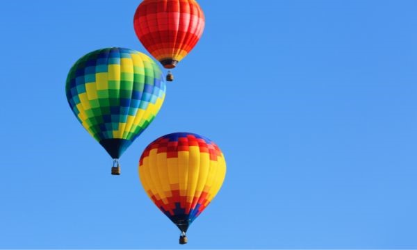 Three colorful hot air balloons, red, yellow, green, and blue, float against a clear blue sky.