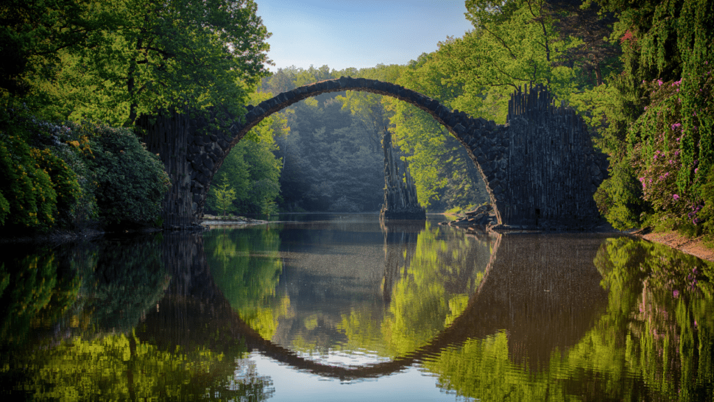 Rakotzbrücke bridge reflected in water, surrounded by lush green trees in Kromlau Park.