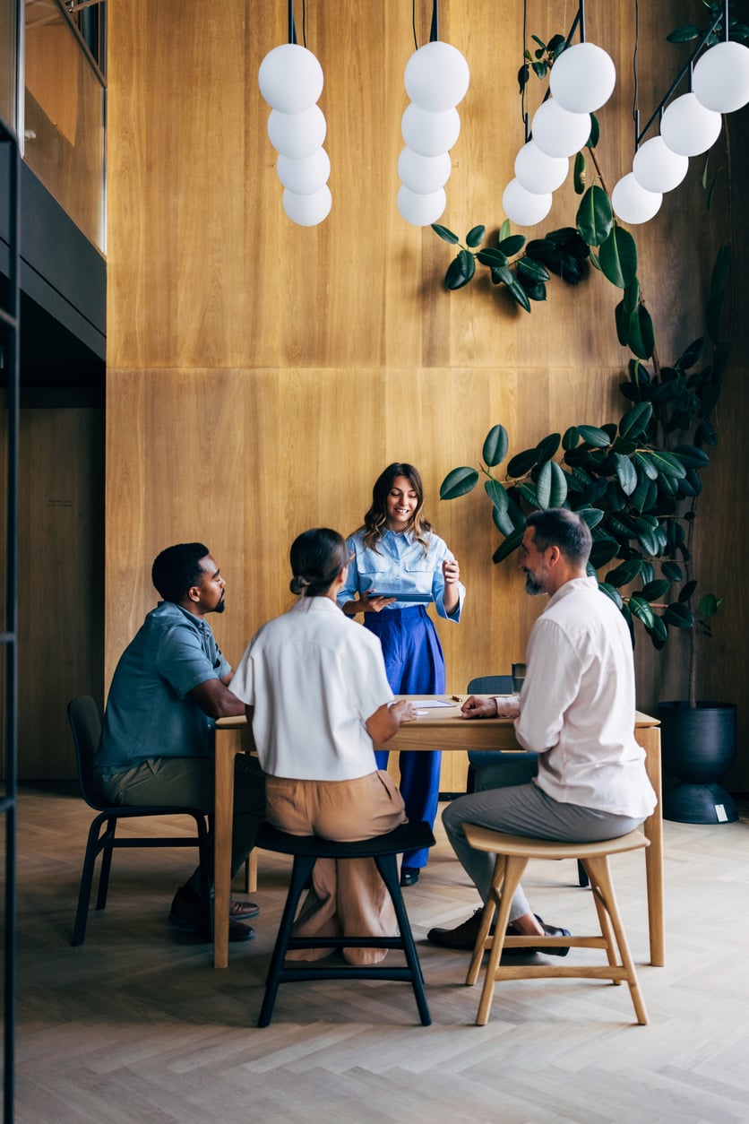 Diverse team meeting in modern office with wooden walls and hanging light fixtures.