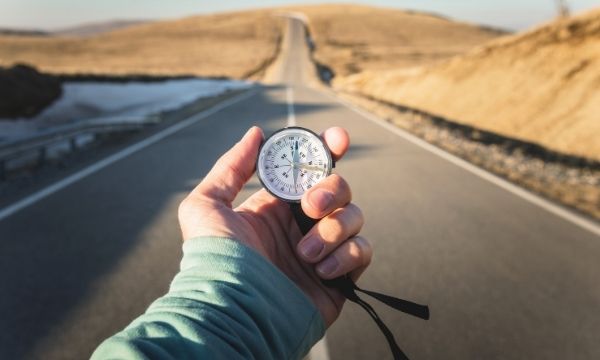 Person holding compass on empty road in desert landscape, seeking direction