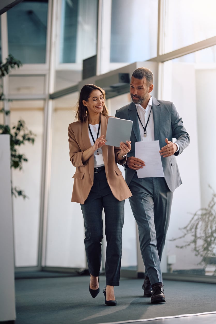 Business colleagues walk and discuss while looking at a tablet and papers in a modern office.