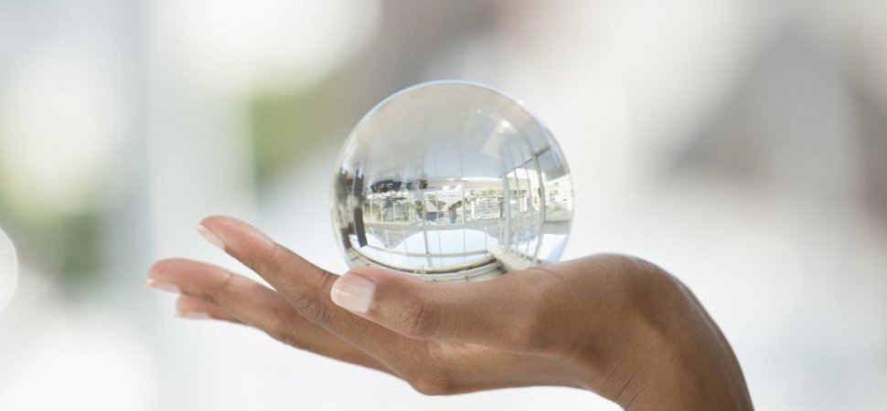 Close-up of a hand holding a clear crystal ball showing a reflection of a modern building interior.