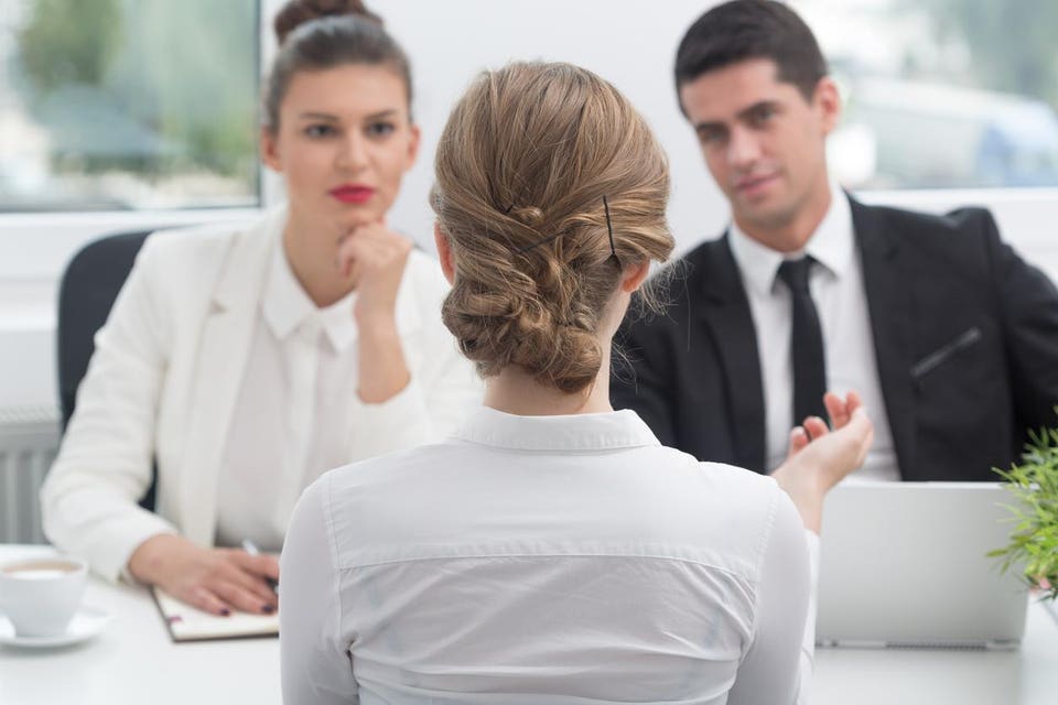 Three professionals in an office meeting: two interviewers and one interviewee.