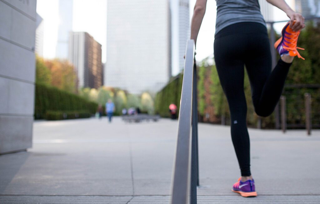Runner stretching quadriceps on outdoor stairs with city buildings in background