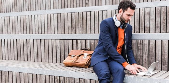 Businessman with headphones and briefcase works on laptop on wooden stairs